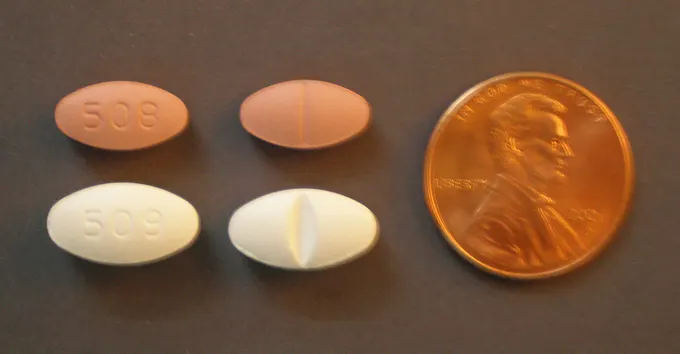 Four oval tablets on a dark surface beside a one cent coin: two coral-coloured 20 mg tablets on top and two white 40 mg tablets below, each shown front and back