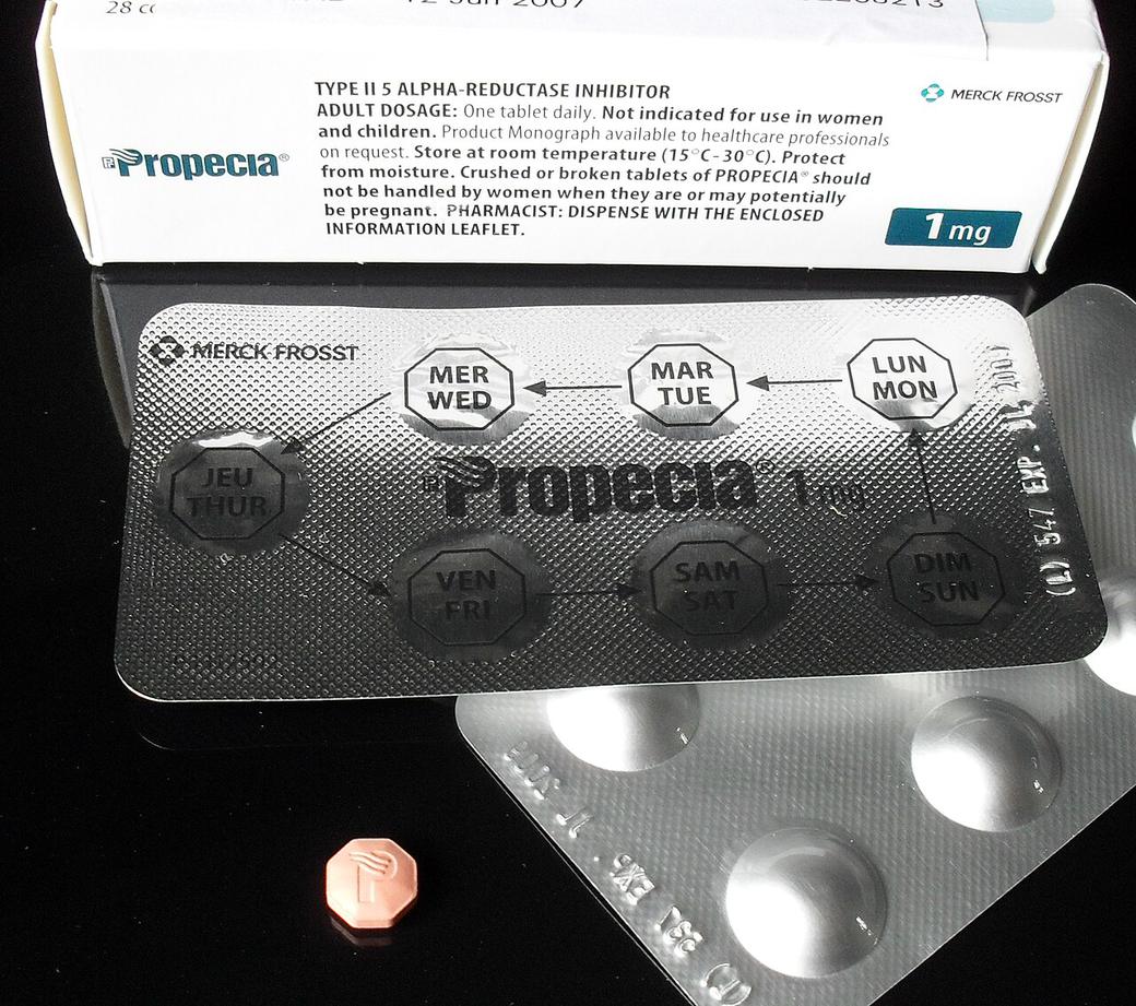 A Propecia 1 mg finasteride carton with a foil blister strip marked with days of the week and one small tablet in front